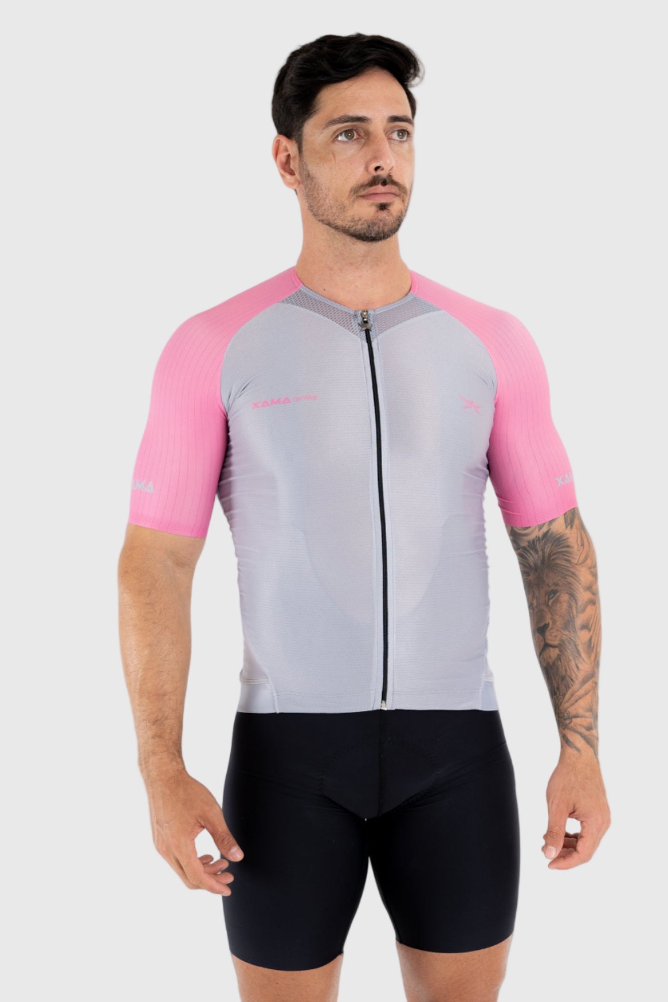 A man wearing a pink and gray cycling top with short sleeves and a front zipper, paired with black cycling shorts.