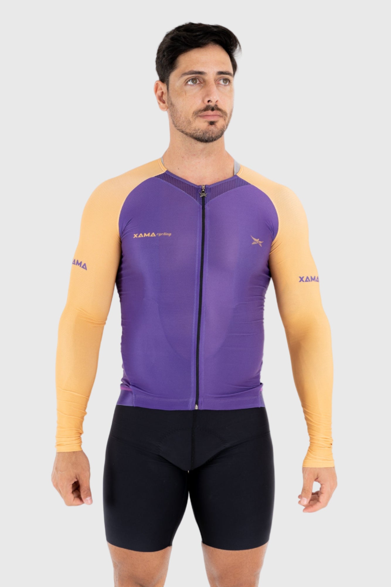A man wearing a purple and gold cycling top with short sleeves and a zipper in the front. The brand logo 'Xama' is visible on the top.