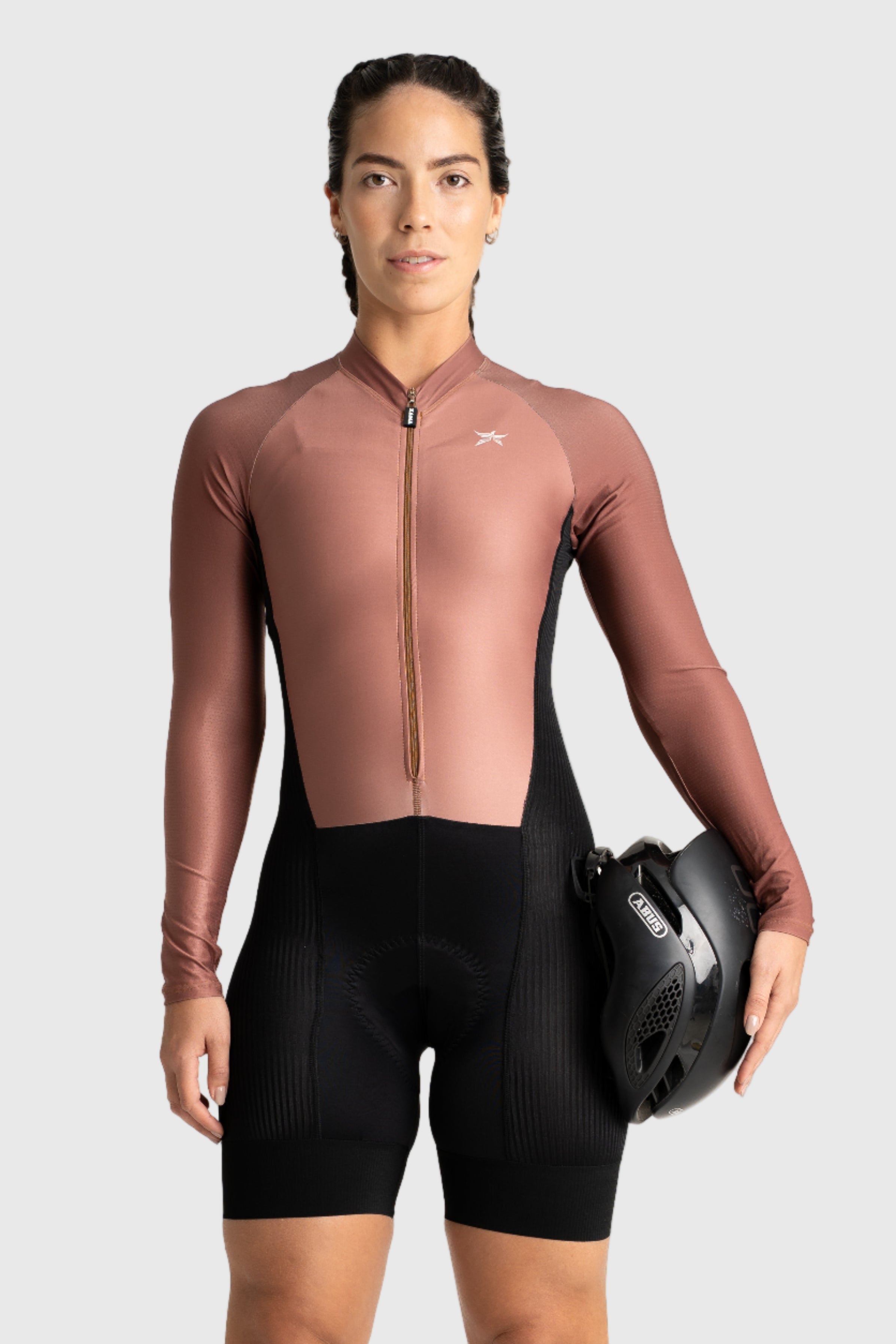 Person wearing a brown cycling suit holding a helmet on a white background