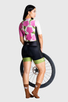 Woman wearing a floral cycling jersey and black bib shorts with a bicycle wheel on a white background