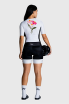 Person wearing a white cycling jersey with floral design and black shorts on a white background