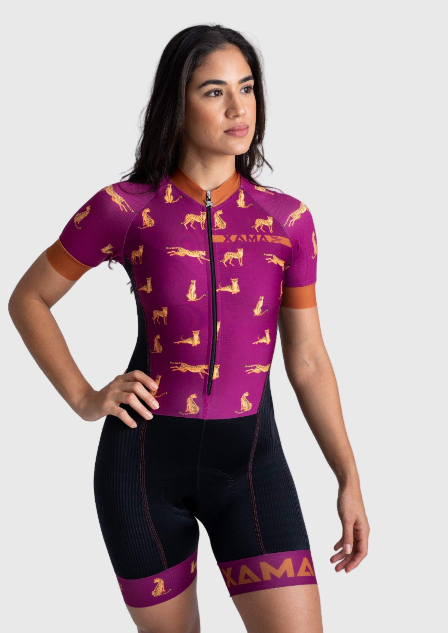 A woman wearing a purple cycling jumpsuit with a jaguar pattern and the brand name 'Xama' on the shorts.