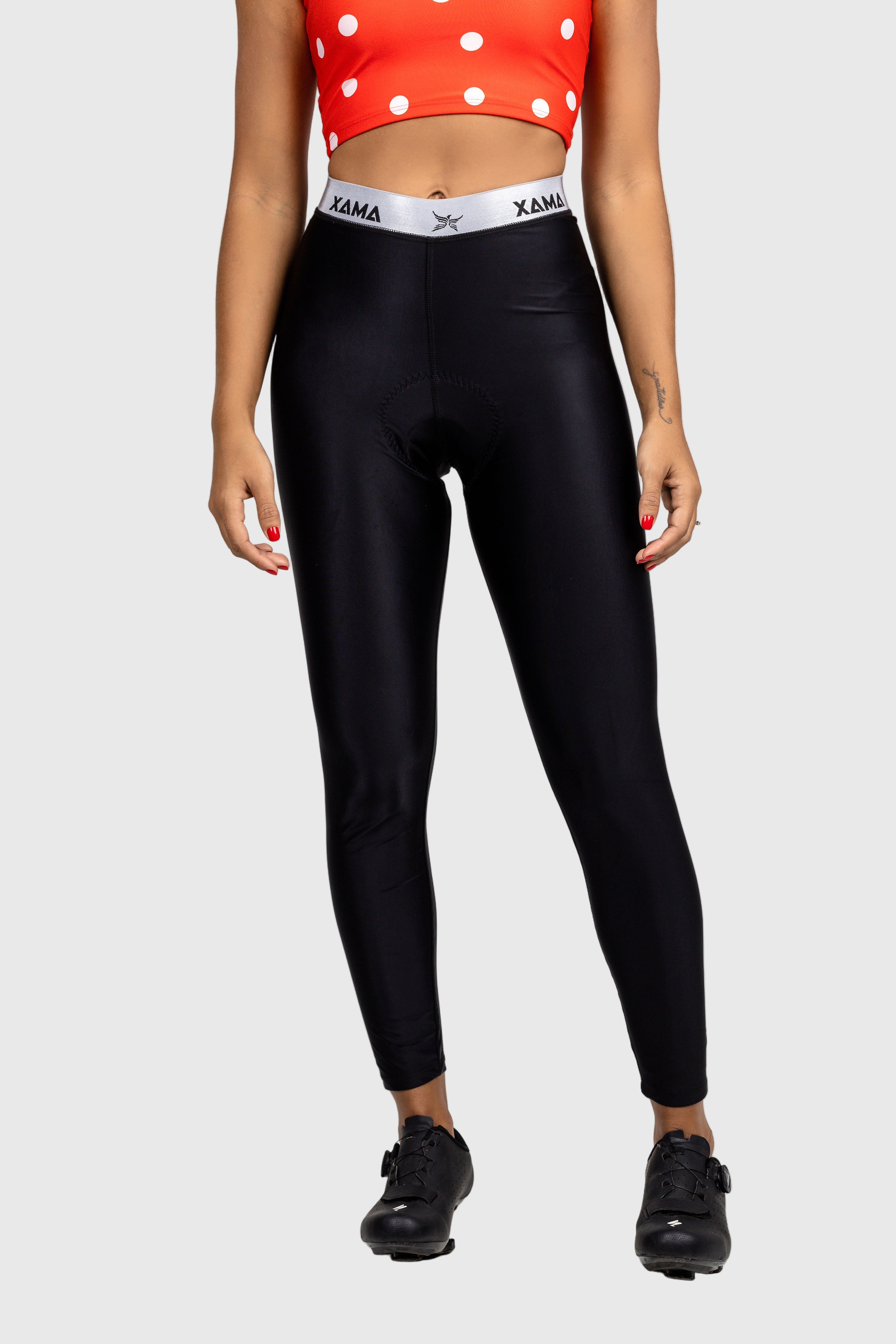 A pair of women's pants with a black color scheme, featuring a high waist and a branded elastic band at the waist. The pants are paired with a dotted orange top and black sports bra visible in the background.